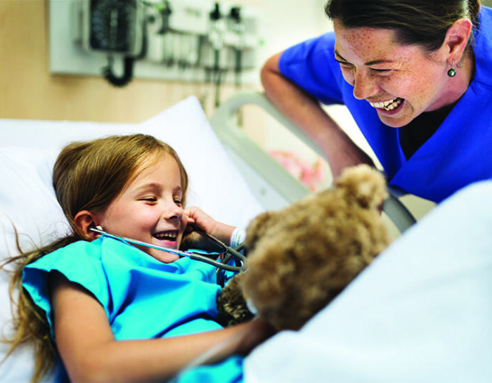 Nurse laughing with a young patient laying down in a hospital bed.